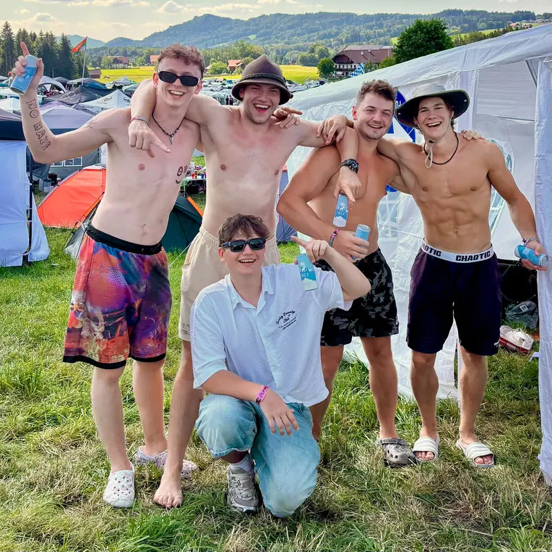 Gruppe von Freunden mit IBEX-Dosen vor Zelten auf einer Festivalwiese